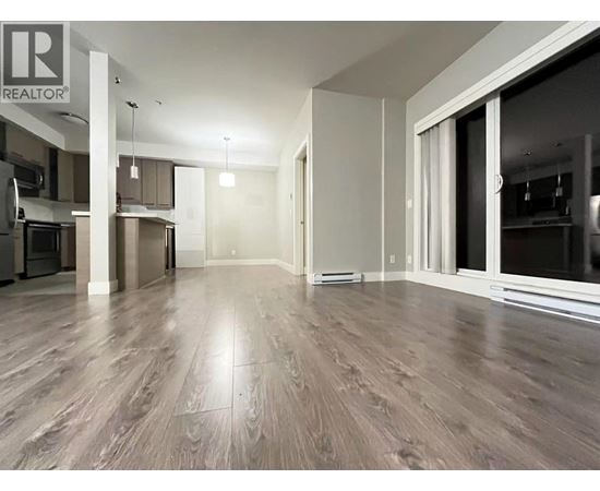 A spacious living room with wood flooring and a kitchen area in the background.