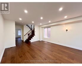 A spacious room with wooden floors and a staircase leading to another level.