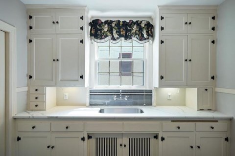 A kitchen with white cabinets and a window with a floral valance.