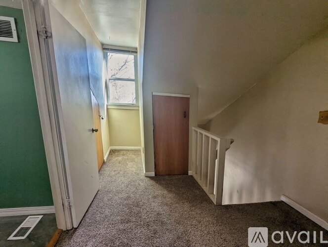 A hallway with a carpeted floor, a door, and a window with a view of trees outside.