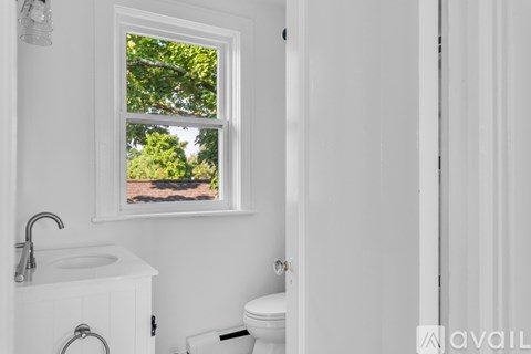 A white bathroom with a window showing trees outside.