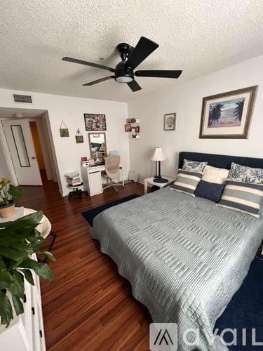 A bedroom with a bed, a ceiling fan, and a nightstand with a lamp.