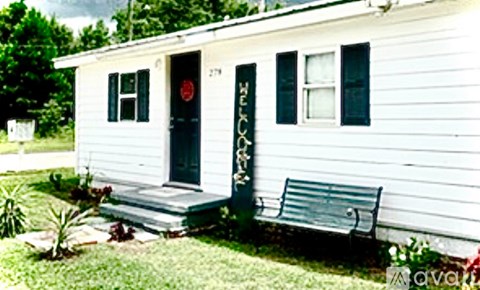 A white house with a black door and a bench in front.
