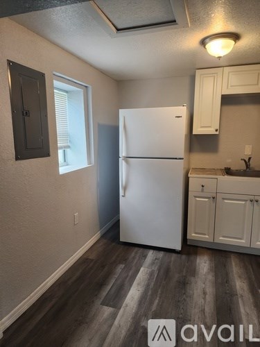 A white refrigerator in a kitchen with wooden floors and white cabinets.