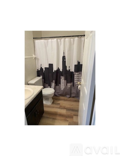 A bathroom with a toilet, sink, and a shower curtain with a city skyline design.
