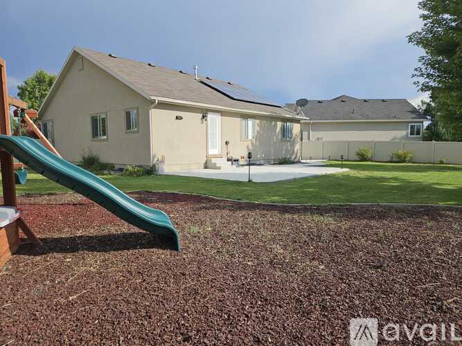 A playground with a green slide in front of a house.