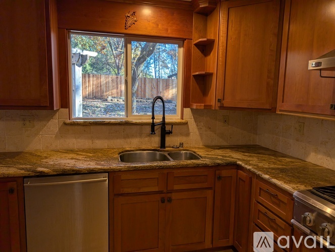 A kitchen with wooden cabinets and a window overlooking a backyard.
