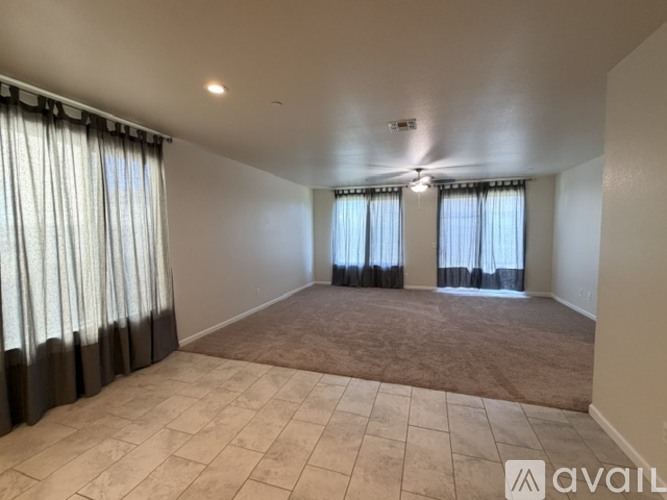 A spacious room with beige carpet and large windows with curtains.