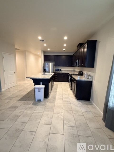 A kitchen with black cabinets and a white trash can.