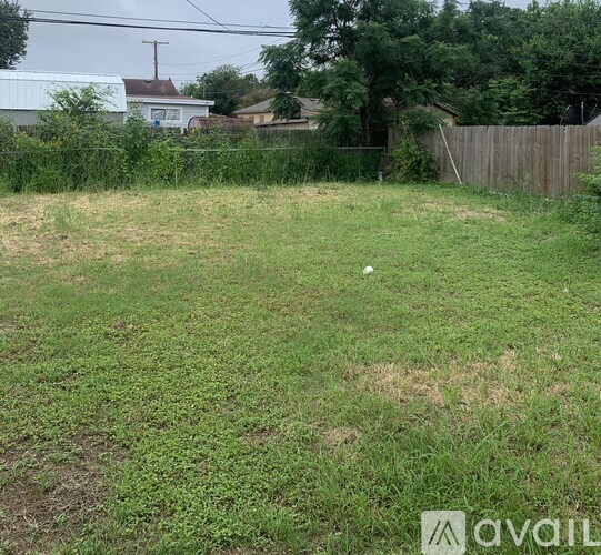 A grassy field with a fence and trees in the background.