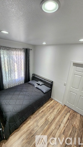 A bedroom with a bed, wooden floor, and a window with curtains.