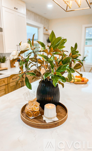 A black vase with a white candle and a white flower sits on a wooden tray.