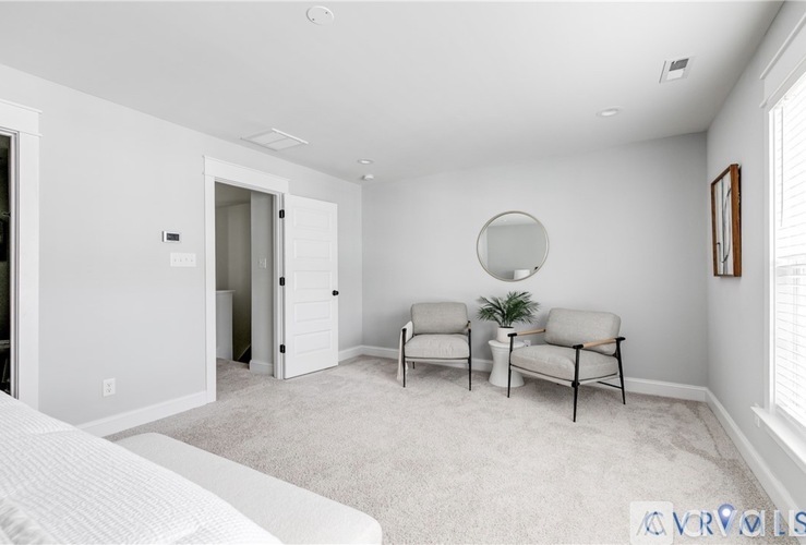 A white bedroom with a bed on the left and a chair and sofa set on the right.