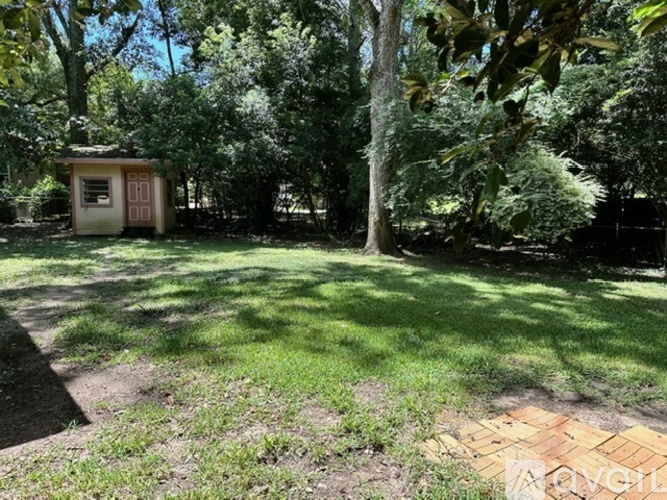 A small house is surrounded by trees and grass in a yard.