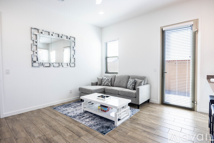 A living room with a grey couch, a white coffee table, and a mirror on the wall.