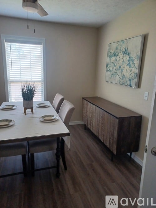 A dining room with a table set for four and a painting on the wall.