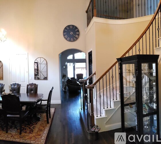 A living room with a dining table and chairs, a staircase, and a clock on the wall.