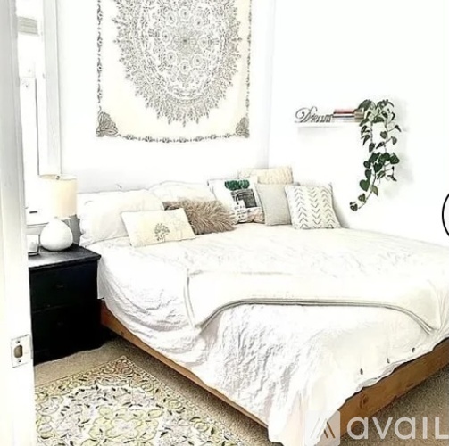 A bedroom with a white bed and a large tapestry on the wall.