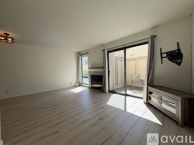 A spacious room with wooden flooring and a sliding glass door leading to a balcony.
