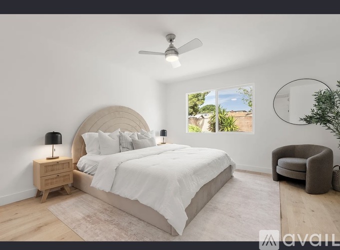 A bedroom with a large bed, a ceiling fan, and a window with a view of the outdoors.