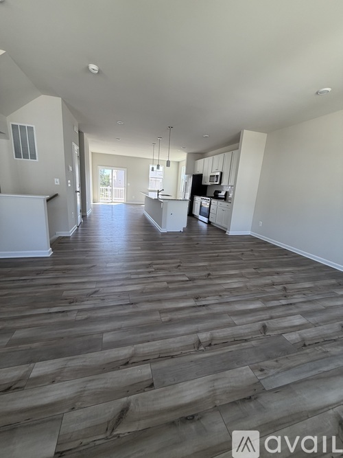 A spacious living room with hardwood floors and a kitchen in the background.