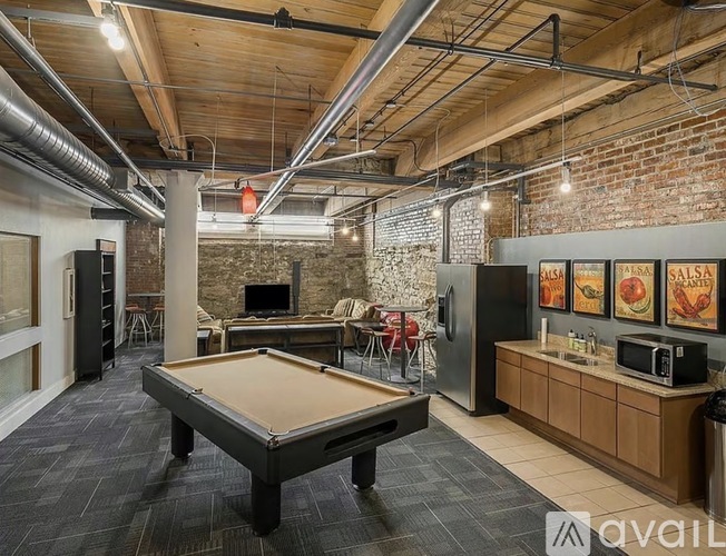 A pool table is in the middle of a room with a brick wall and a bar area.