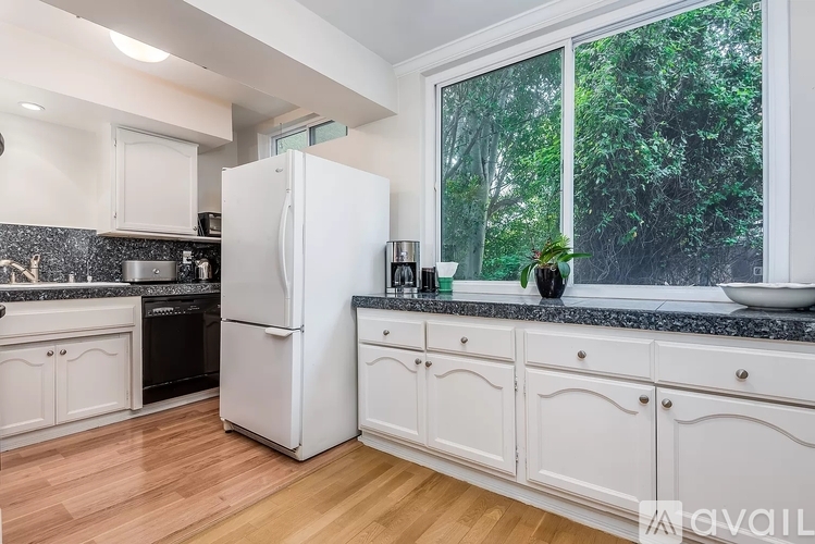 A white refrigerator stands in a kitchen with wooden floors and white cabinets.