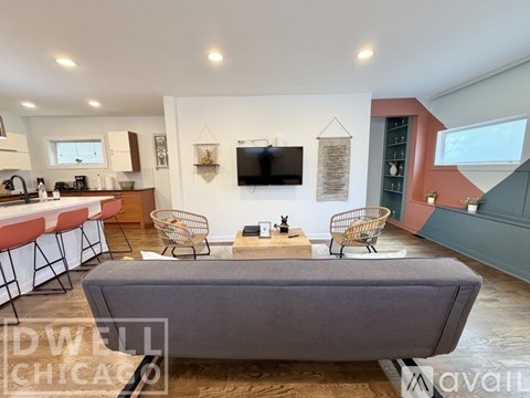 A modern living room with a grey sofa and a kitchen area in the background.