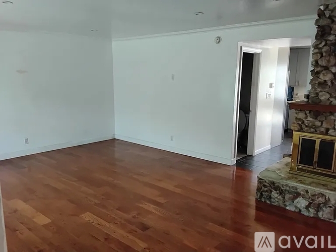 A room with wooden flooring and a stone fireplace.