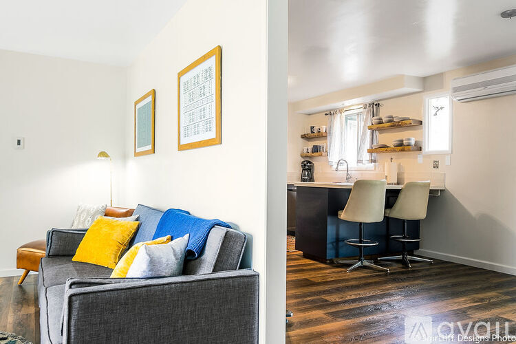 A living room with a grey couch and a kitchen area in the background.