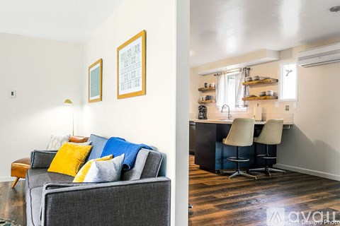 A living room with a grey couch and a kitchen area in the background.
