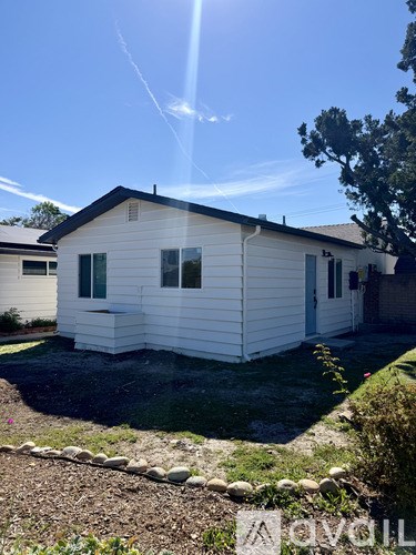 A small white house with a black roof and a green window.