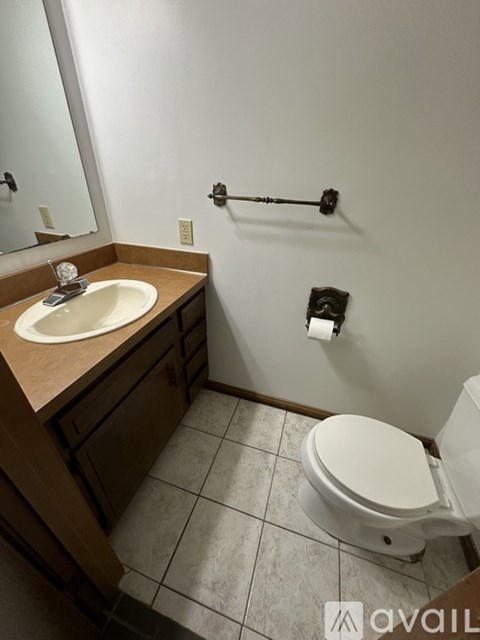 A bathroom with a toilet, sink, mirror, and towel rack.