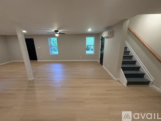 A spacious room with wooden flooring and a staircase on the right side.