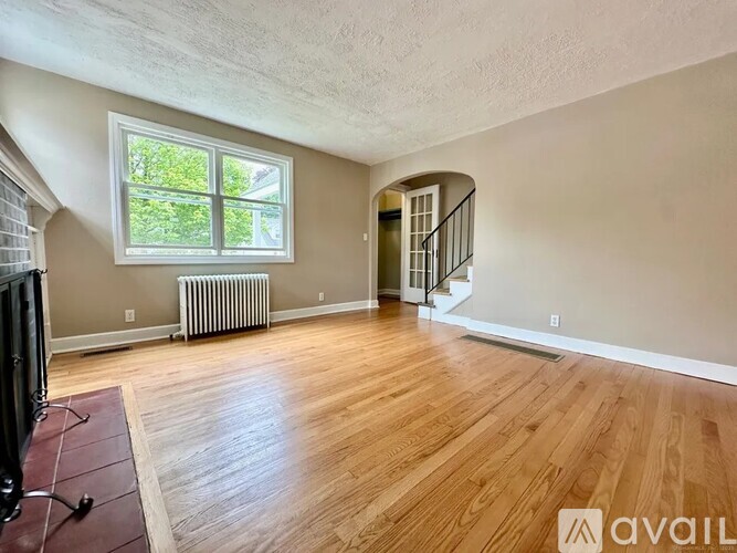 A spacious room with wooden flooring and a staircase.