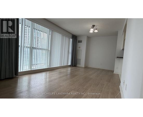 A room with wooden flooring and a large window with blinds.