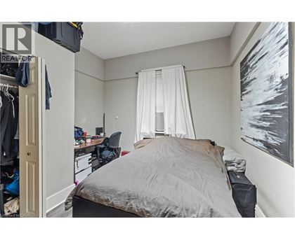 A bedroom with a bed, desk, chair, and a painting on the wall.