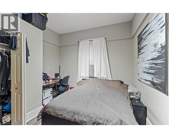 A bedroom with a bed, desk, chair, and a painting on the wall.