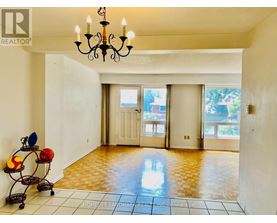 A room with a chandelier, a table with a vase and a bowl, and a brokerage logo on the wall.