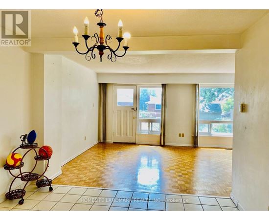 A room with a chandelier, a table with a vase and a bowl, and a brokerage logo on the wall.