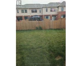 A grassy yard in front of a brown fence and apartment building.