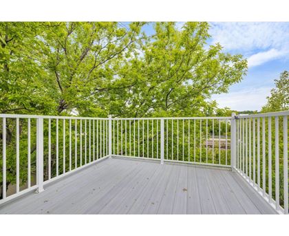 A white deck with a railing and trees in the background.