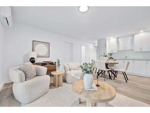 A living room with a white couch, a wooden coffee table, and a dining table with chairs.