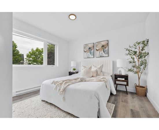 A white bedroom with a large bed and a potted plant.