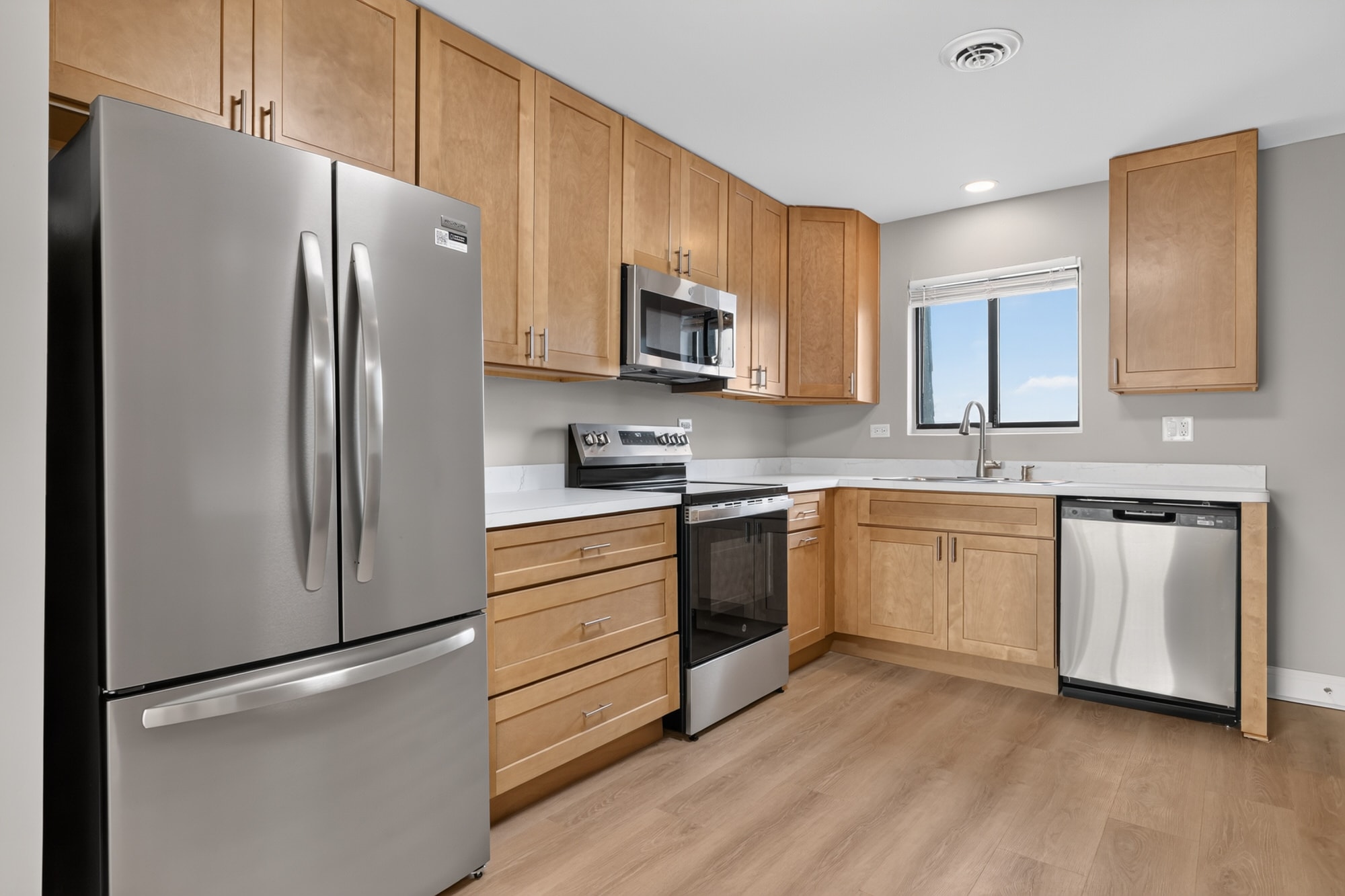 A kitchen with a refrigerator, oven, microwave, dishwasher, and sink.