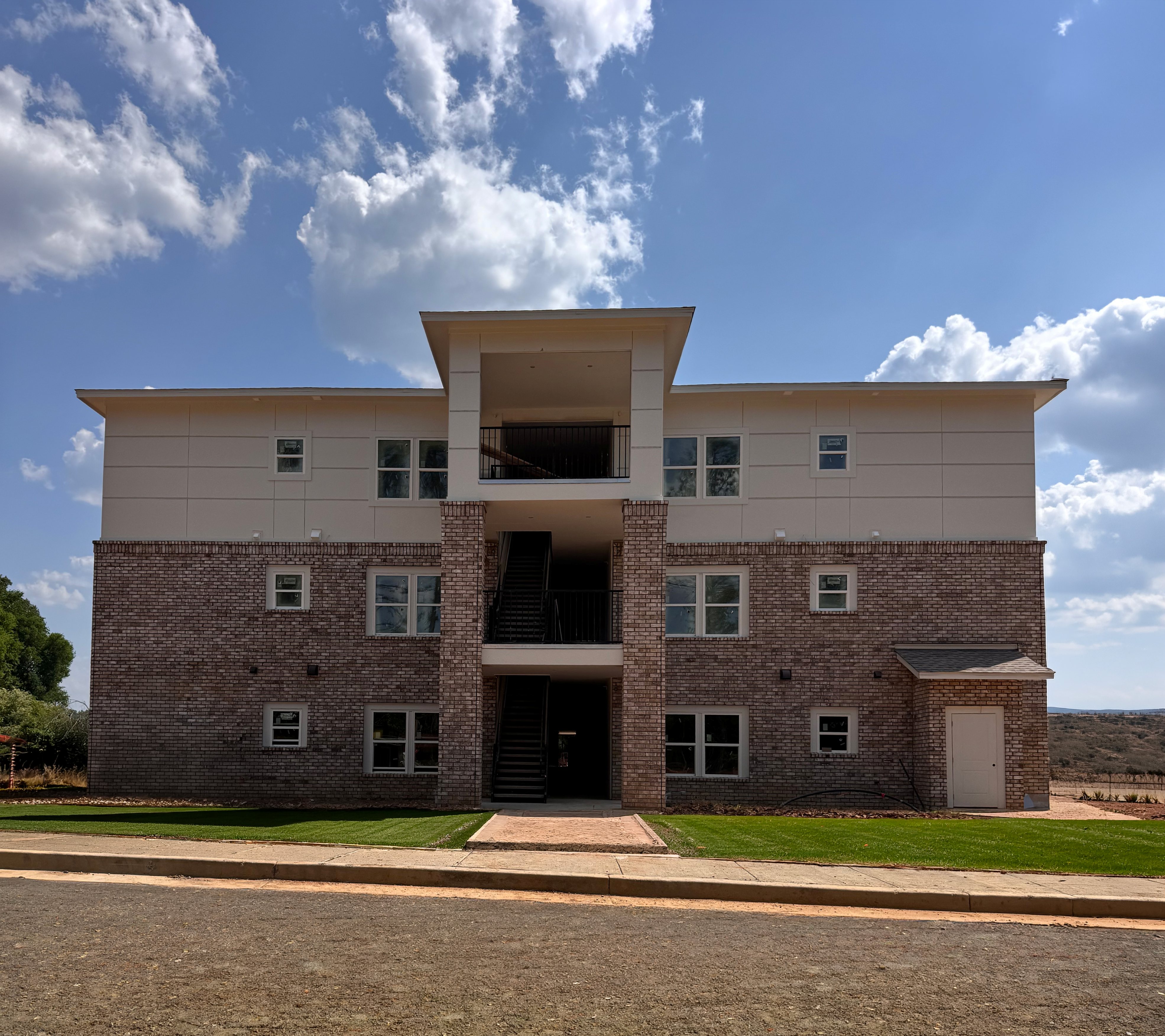 A modern two-story building with a flat roof and a balcony on the second floor.