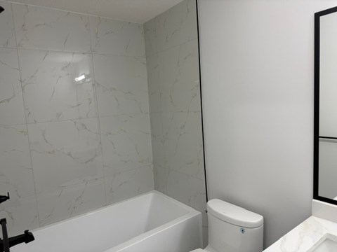 A white toilet sits next to a white bathtub in a bathroom.