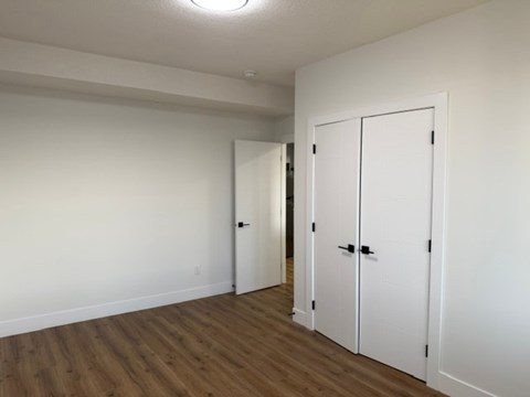 A room with white walls and wooden flooring, featuring a white door and a white wardrobe with black handles.