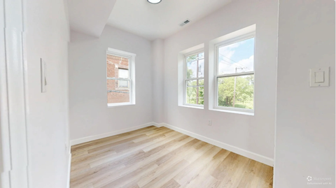 A room with white walls and wooden flooring, with a window showing a view of trees and a building.