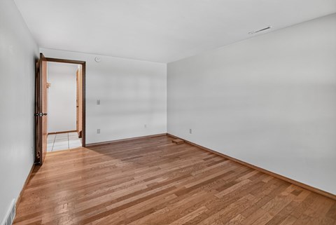 A room with wooden flooring and a white wall with a door.